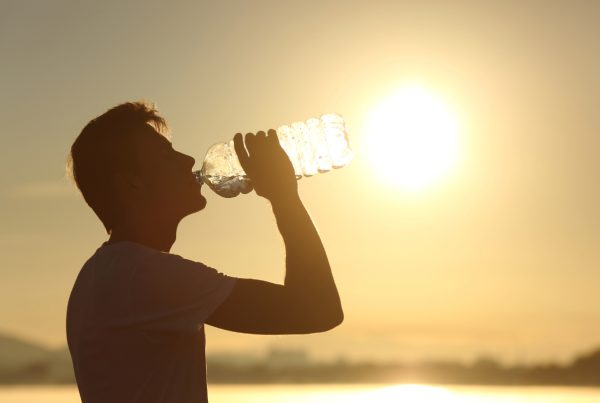 Homem a beber garrfa de água com sol abrasador ao fundo